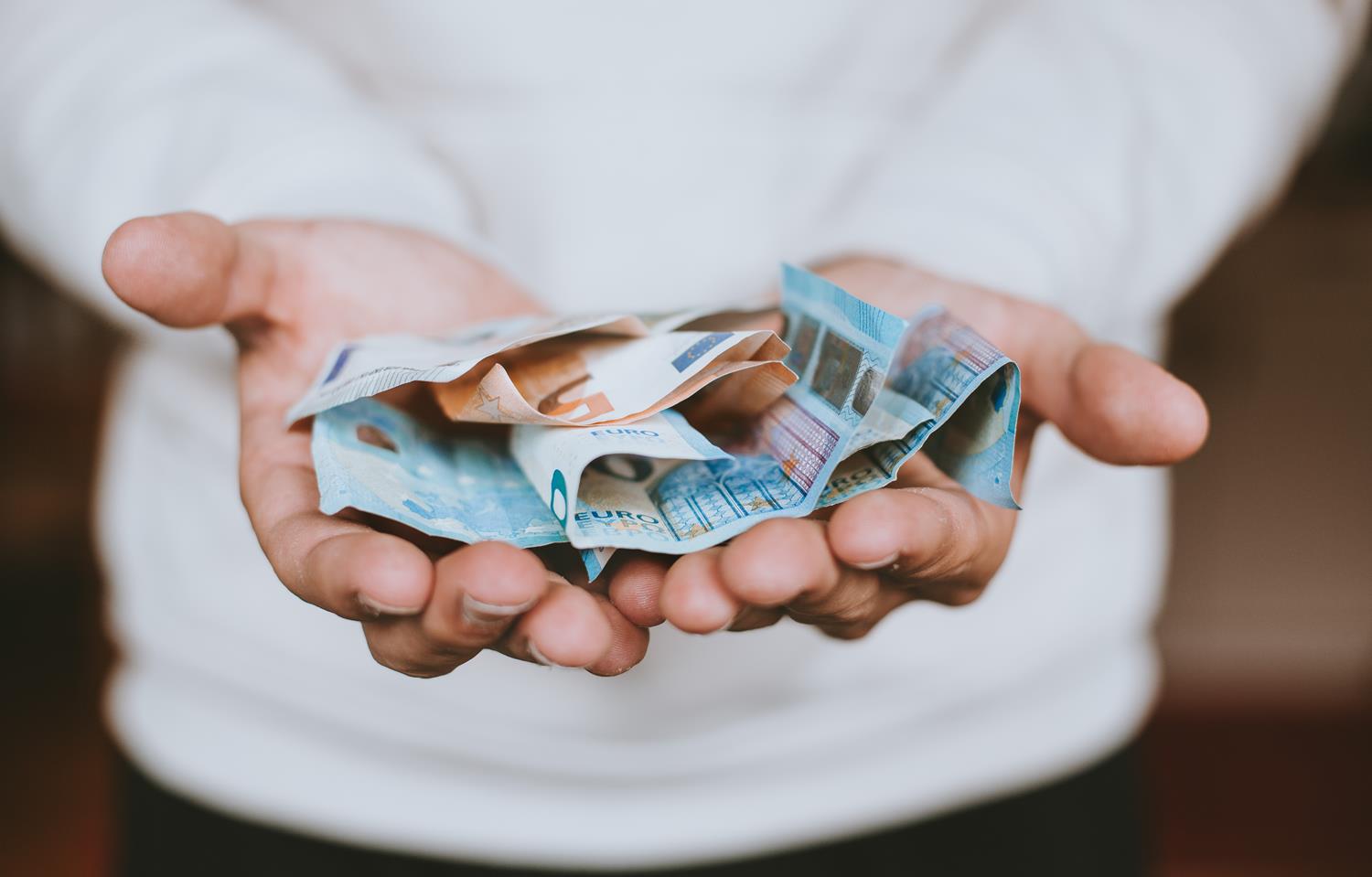 Man with his hands out holding a fist-full of money